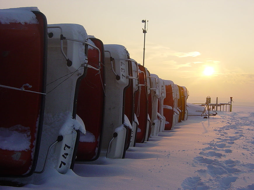 Row of red and white boats covered in snow at sunset
