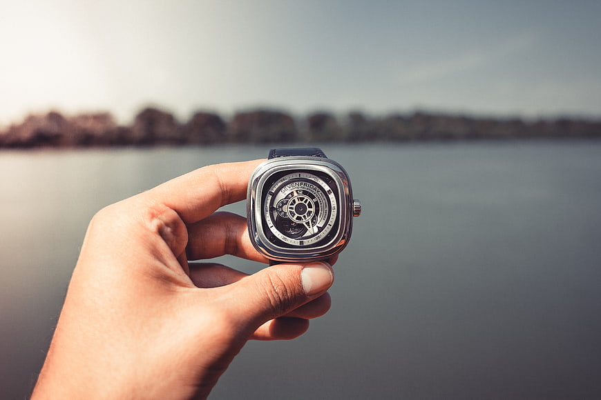 Hand holding luxury skeleton watch by the water