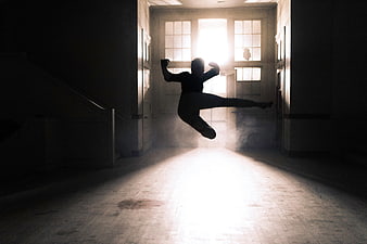 Silhouette of man performing high kick in dark hallway