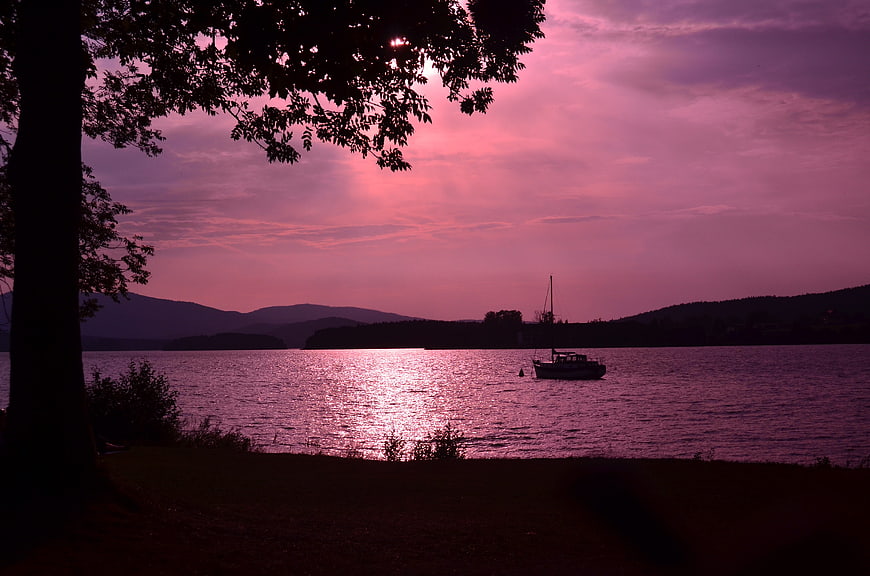Serene Lake Sunset with Silhouetted Boat and Tree