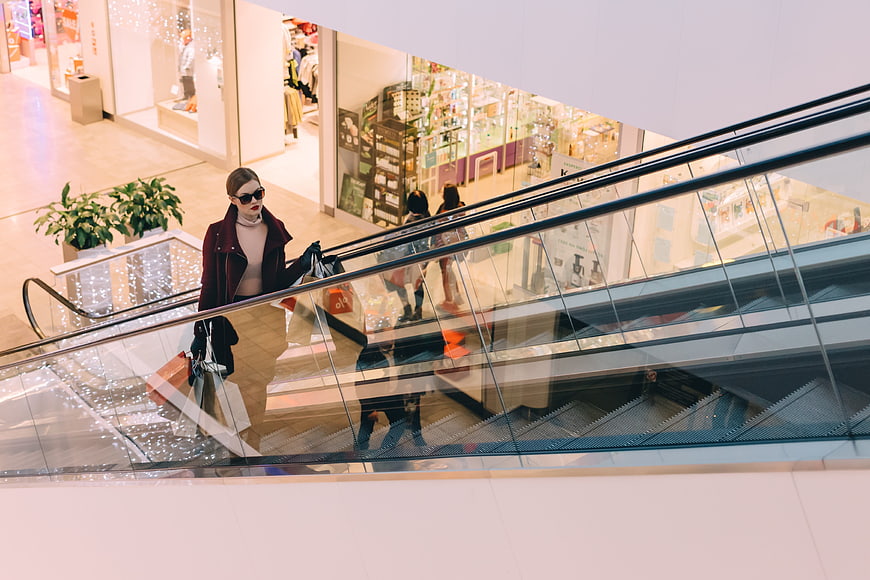 Fashionable woman with shopping bags on escalator in mall