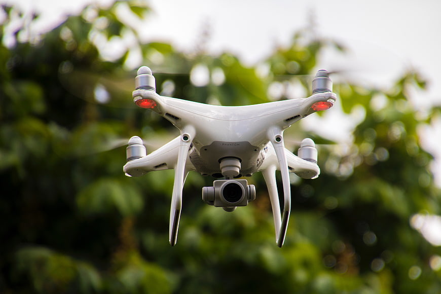 White drone hovering in front of green trees