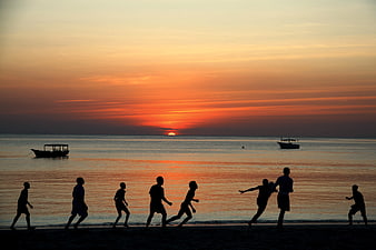 Silhouettes of People Playing Soccer on Beach at Sunset