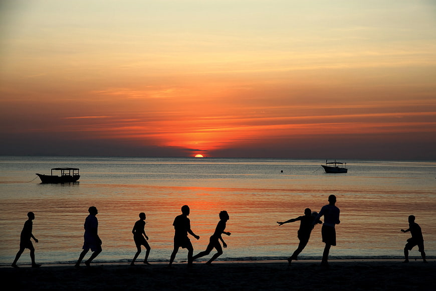 Silhouettes of People Playing Soccer on Beach at Sunset