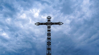 Ornate metal cross silhouette against dramatic cloudy blue sky