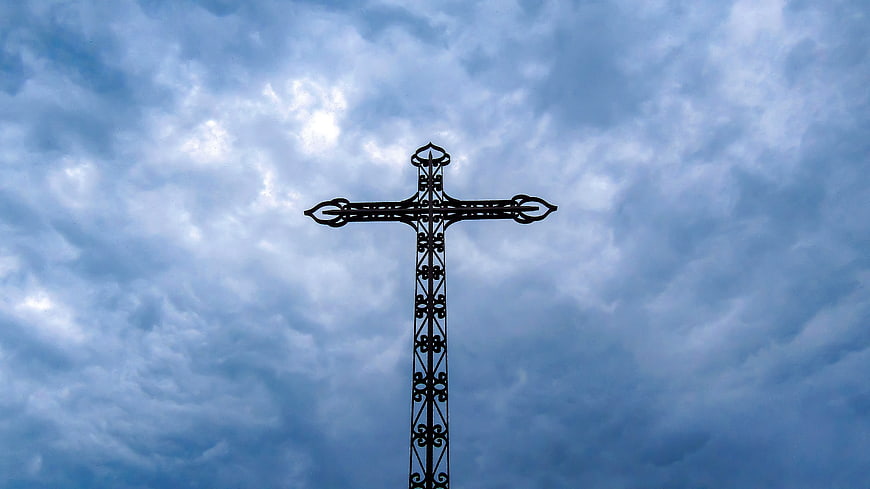 Ornate metal cross silhouette against dramatic cloudy blue sky