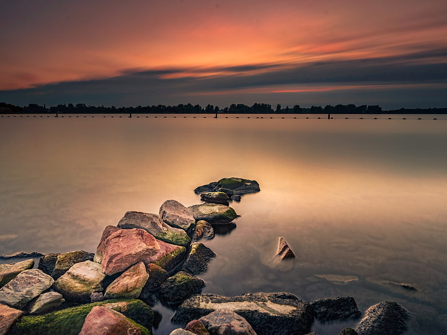 Long exposure sunset over calm water with mossy rocks