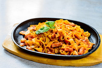 Hot skillet pasta with sausage and basil on wooden board