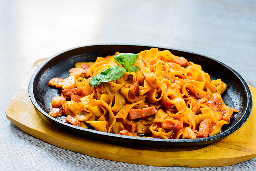 Hot skillet pasta with sausage and basil on wooden board