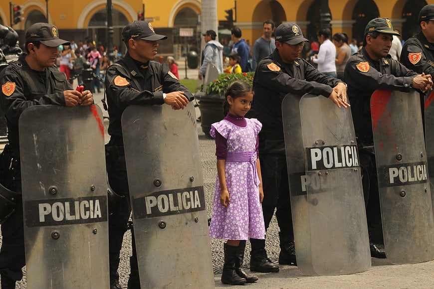 Young girl in purple dress standing before Peruvian police riot shields