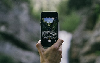 Hand holding smartphone photographing waterfall in nature