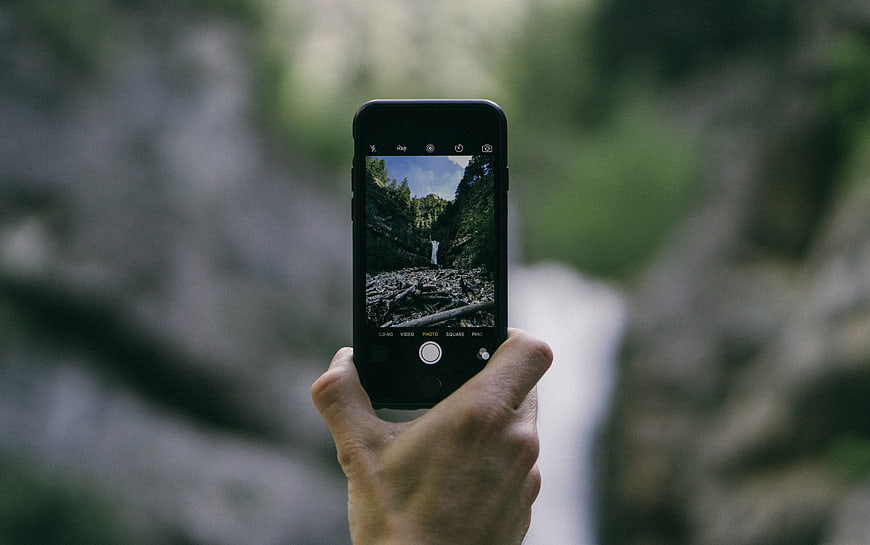 Hand holding smartphone photographing waterfall in nature