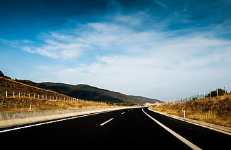 Empty asphalt highway curving through dry hills under blue sky