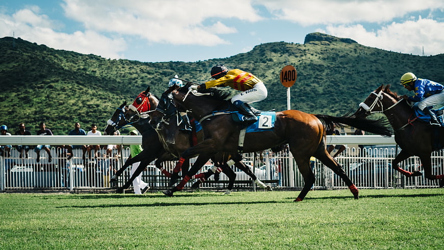 Horse Racing Action on Grassy Track with Mountain Background