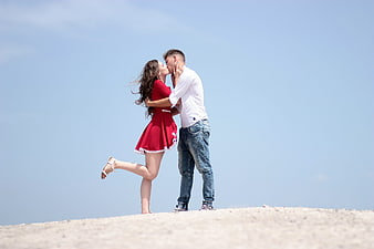 Romantic couple kissing on a sandy hill against a clear blue sky