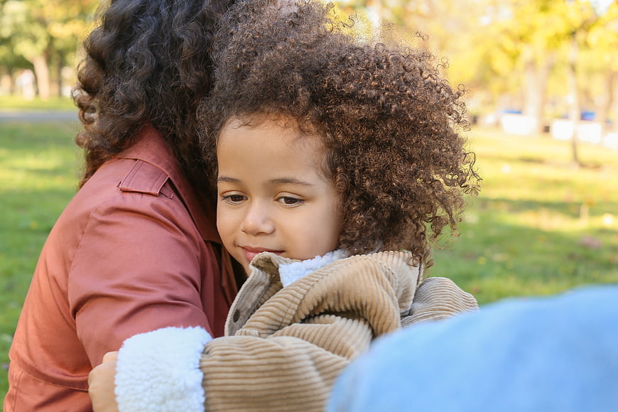 Cute child with curly hair hugging adult outdoors