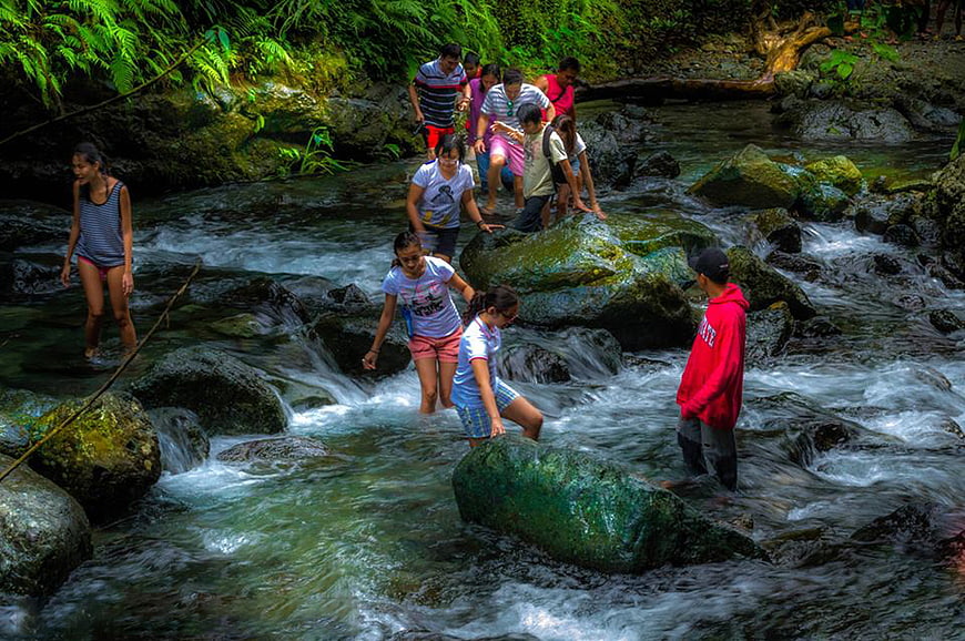 Group of friends hiking and crossing a rocky stream in nature