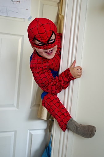Happy child in Spider-Man costume peeking around door frame