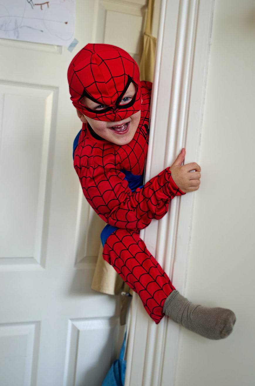 Happy child in Spider-Man costume peeking around door frame