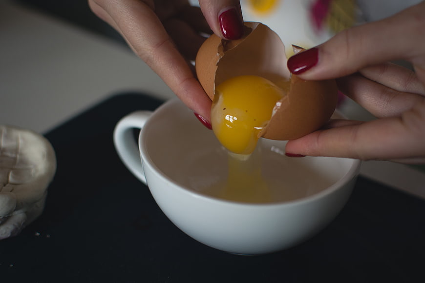 Close-up of hands cracking a fresh egg into a white bowl