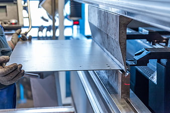 Worker bending metal sheet on industrial press brake machine