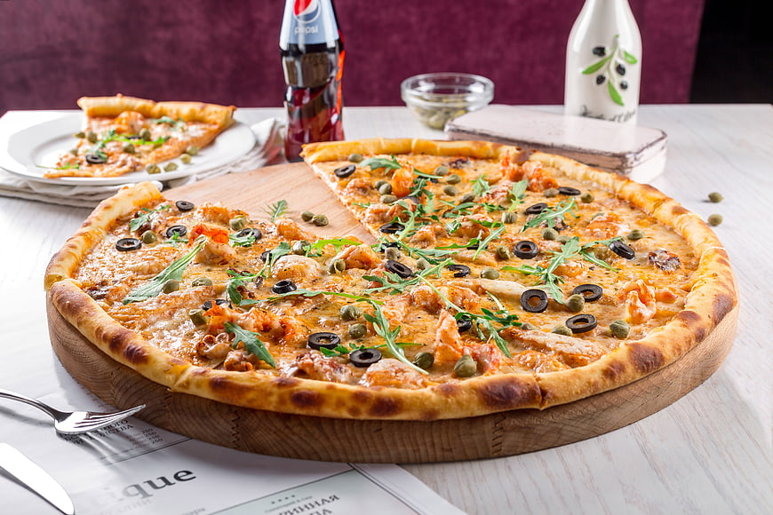 Delicious Pizza with Shrimp, Olives, and Arugula on Wooden Board