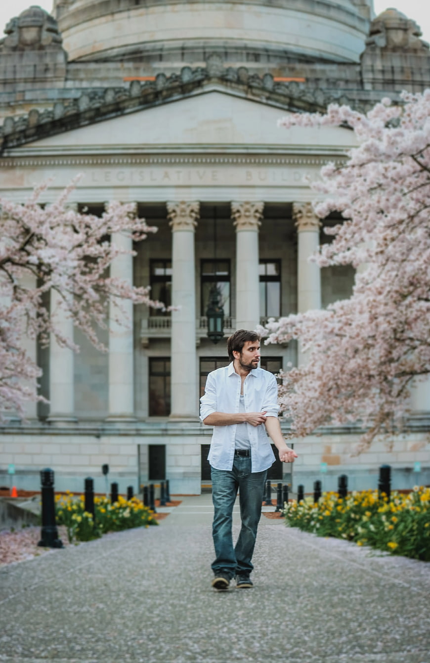 Man in White Shirt Walking Past Legislative Building with Cherry Blossoms
