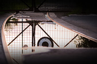 Reflection of fence and sunset in puddle on railroad tracks