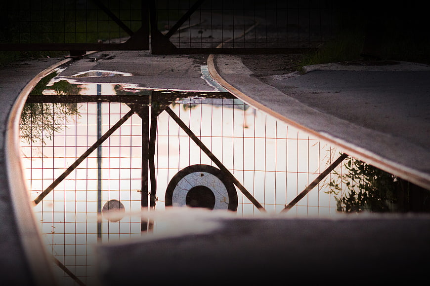 Reflection of fence and sunset in puddle on railroad tracks