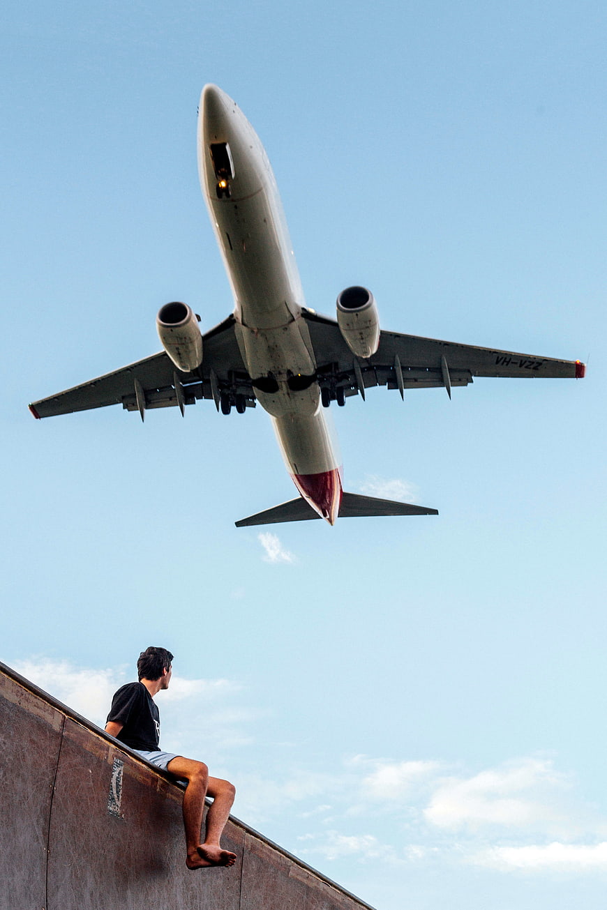 Man watching airplane fly overhead against blue sky