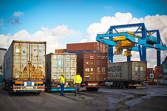 Shipping containers and workers at a busy port with large blue crane