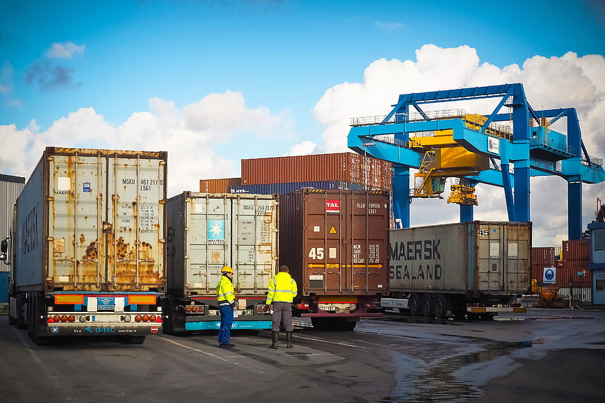 Shipping containers and workers at a busy port with large blue crane