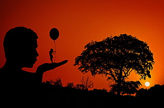 Silhouette of man holding tiny child with balloon at sunset