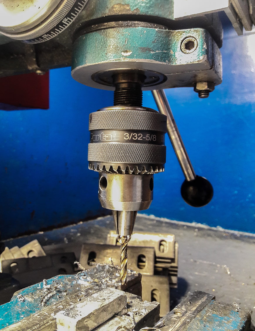 Close-up of drill press chuck and bit on metal workpiece