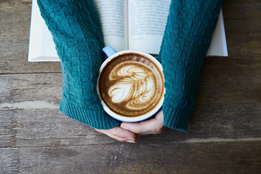 Hands holding latte art coffee mug over open book