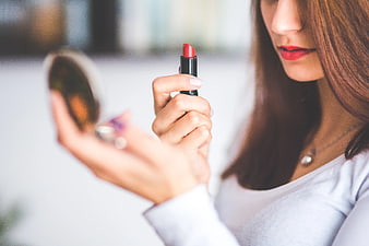 Woman applying red lipstick while looking in a compact mirror