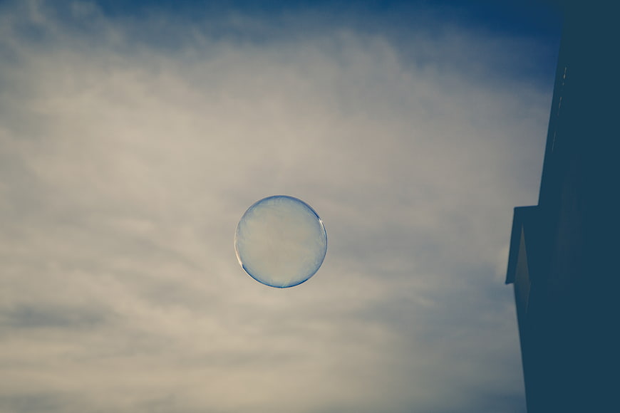 Single soap bubble floating against cloudy sky