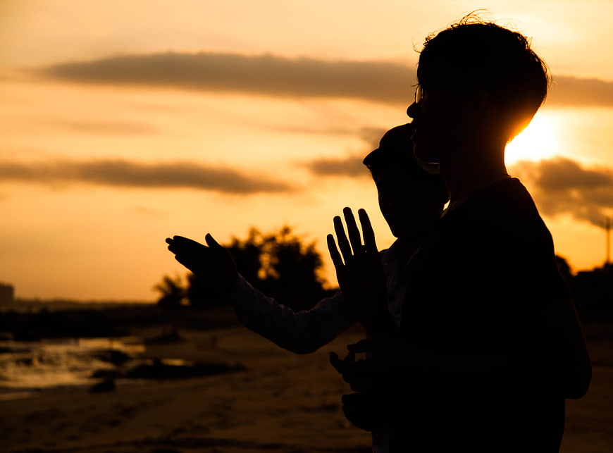 Silhouette of couple praying on beach at sunset