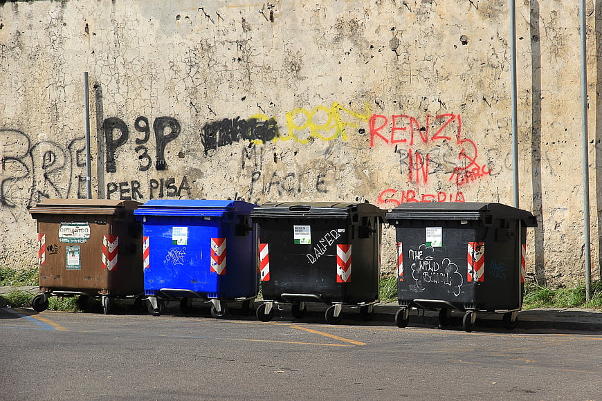 Row of four wheeled waste bins lined up against a graffiti-covered concrete wall