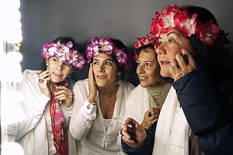 Four women wearing floral crowns looking into a vanity mirror