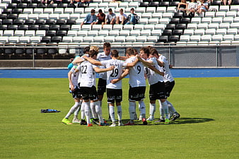 Soccer Team Huddle On Green Pitch With Stadium Background