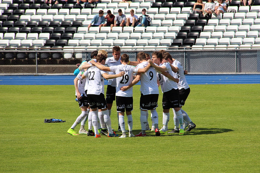 Soccer Team Huddle On Green Pitch With Stadium Background