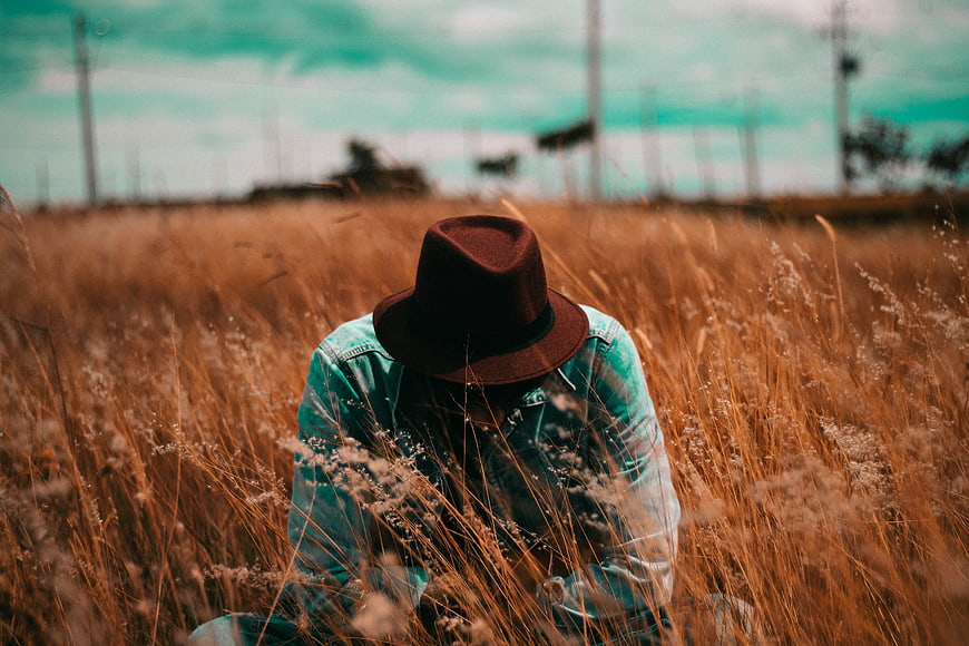 Man in Fedora Sitting in Dry Grass Field