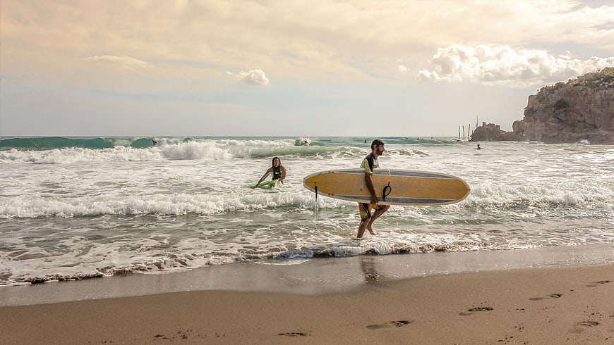 Surfer walking on beach with yellow surfboard