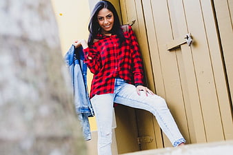 Stylish Woman in Red Plaid Shirt and Jeans Leaning Against Wall