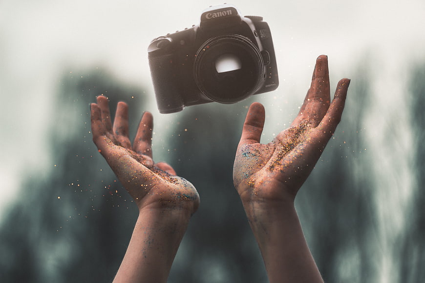 Hands holding floating DSLR camera with magical particles