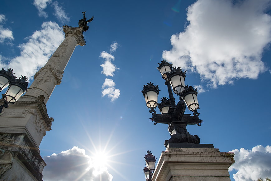 Low angle view of monument column and lamp post against blue sky