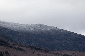 Snow-Capped Mountain Ridge with Forested Slopes Under Overcast Sky
