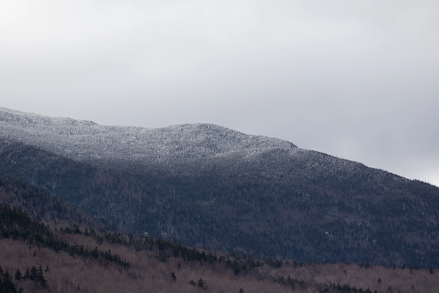 Snow-Capped Mountain Ridge with Forested Slopes Under Overcast Sky