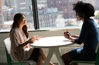 Two women having a conversation at a table by a window